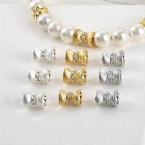 Puede incluir: Un conjunto de diez separadores de cuentas en forma de lazo de oro y plata con diamantes de imitación transparentes. Los separadores están diseñados para ser utilizados en la elaboración de joyas.