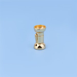 May include: A gold-colored metal furniture leg with a decorative design. The leg has a round base and a cylindrical shaft with a decorative cap.