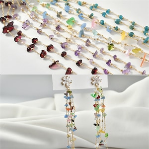 Può includere: Un set di collane a catena dorata con perline di pietre preziose di vari colori. Le collane sono esposte su una superficie bianca. Ci sono anche due orecchini dorati con un design a fiore e una catena pendente di perline di pietre preziose colorate.