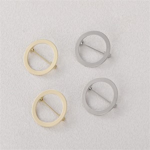 Pode incluir: Quatro broches circulares, dois dourados e dois prateados, com um pino na parte de trás. Os broches são simples e elegantes, com um centro oco.