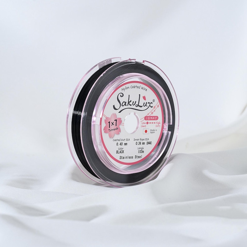 May include: A spool of black nylon-coated wire, labeled "SakuLux", with a pink and white label. The label indicates a 0.40 mm coated outer diameter and a 0.24 mm inner rope diameter. The wire is 100 meters long and made of stainless steel.