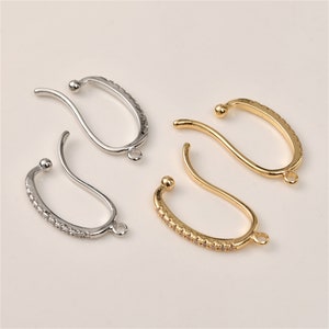 Op de afbeelding: Vier oorhaakjes met een gebogen ontwerp. Twee zijn zilverkleurig met heldere strass steentjes en twee zijn goudkleurig met heldere strass steentjes.