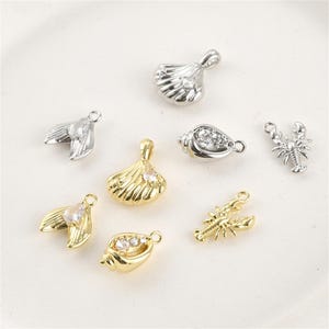 May include: A collection of small, decorative charms in gold and silver tones. The charms include seashell, mermaid tail, and lobster designs, some with clear crystal accents. These charms are ideal for jewelry making.