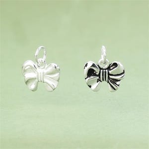 Op de afbeelding: Twee zilveren strikcharms met een lus aan de bovenkant om aan een ketting of armband te bevestigen.