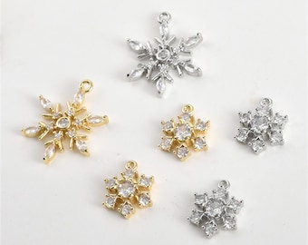 Könnte beinhalten: Sechs silberne und goldene Schneeflocken-Anhänger mit klaren Kristall-Akzenten. Die Anhänger sind perfekt für die Schmuckherstellung oder um handwerklichen Arbeiten einen Hauch von Glanz zu verleihen.