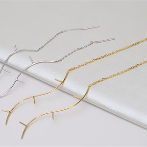 Peut inclure: Deux paires de boucles d'oreilles longues et pendantes. Une paire est en argent avec une chaîne délicate et un motif incurvé en forme de branche. L'autre paire est en or avec une chaîne plus épaisse et un motif incurvé similaire en forme de branche.