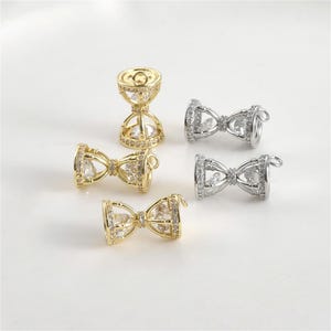 May include: Four gold and silver tone hourglass-shaped jewellery findings with clear crystal accents. The findings are designed to be used as a connector for jewellery making.