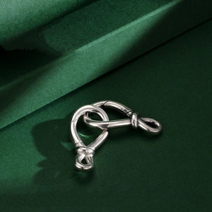 Puede incluir: Cierre de metal plateado con un diseño anudado. El cierre tiene forma de ocho y tiene un acabado liso y pulido.