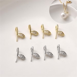 Op de afbeelding: Een set van acht metalen sieradenhangers, vier in goudkleur en vier in zilverkleur, elk voorzien van een bladvormig accent bezet met kleine heldere kristallen en een verticale pin voor het bevestigen van een parel of kraal.