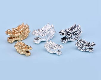 May include: Five silver and gold dragon head charms of varying sizes. The dragon heads are detailed and have a textured finish.
