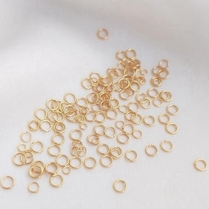 May include: A large quantity of small, gold-colored jump rings. The rings are scattered on a white surface.