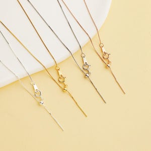 May include: An assortment of fine necklaces in silver, gold, and rose gold. Each necklace has a delicate chain, a sliding bead, and a small pendant. The necklaces are presented against a soft, neutral background.