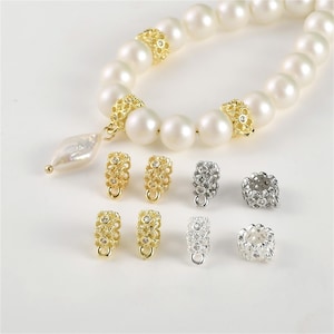 May include: A set of gold, silver, and black metal bead caps with a decorative design. The bead caps have a small loop at the bottom for attaching to a necklace or bracelet.
