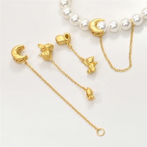 Puede incluir: Un conjunto de dijes dorados con una luna creciente, un corazón, un conejo, un oso y un pajarito. Los dijes están unidos a delicadas cadenas doradas y se pueden usar para decorar una pulsera o un collar.