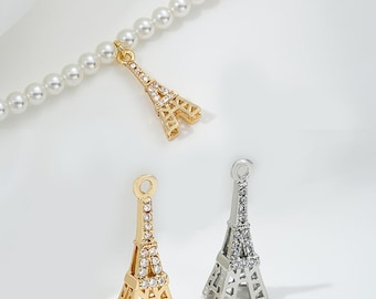 May include: Two Eiffel Tower charms, one gold and one silver, with clear crystal accents. The charms are shown on a pearl necklace.