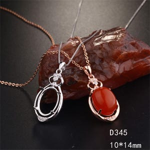 Op de afbeelding: Twee ovale hangerkettingen met kettingen, een zilverkleurige en een roségoudkleurige. De roségouden hanger heeft een gladde, gepolijste rode ovale steen. De zilveren hanger is een lege zetting. Tekst D345 10*14mm is zichtbaar in de hoek.