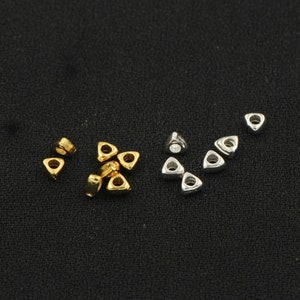 May include: A group of small, triangular metal beads in gold and silver. The beads have a hole in the centre for stringing.