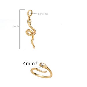 Könnte beinhalten: Zwei goldene Schlangen-Anhänger. Der größere Anhänger ist 3,6 cm lang und hat ein grünes Steinauge. Der kleinere Anhänger ist 4 mm breit und hat ein klares Steinauge.