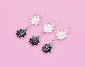 May include: Six silver charm pendants in the shape of a flower. Three of the flowers are white and three are black.