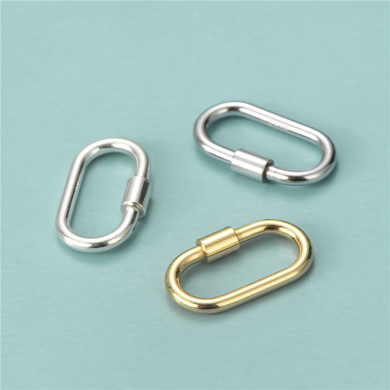 May include: Three oval-shaped carabiner clasps in silver and gold tones. The clasps have a screw-lock mechanism for secure closure. The background is a solid light blue.