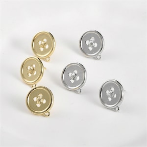 May include: Six button-shaped stud earrings. Three are gold-toned, and three are silver-toned. Each earring features a cross-shaped design in the center and a small loop at the bottom for attaching to a chain or other jewelry component.