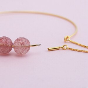 May include: A gold chain bracelet with two pink and white gemstone beads. The bracelet is open and the chain is separated from the beads.