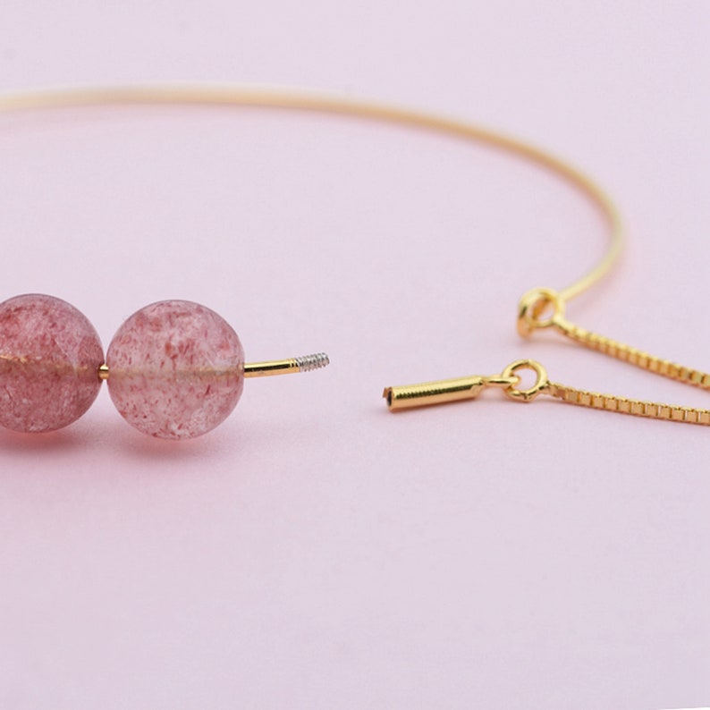 May include: A gold chain bracelet with two pink and white gemstone beads. The bracelet is open and the chain is separated from the beads.