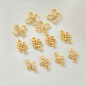 Könnte beinhalten: Eine Sammlung goldfarbener Schmuckzubehörteile, darunter Blumen- und Knotenformen. Die Zubehörteile bestehen aus glänzendem Metall und sind auf einer hellen Oberfläche angeordnet. Diese kleinen Komponenten werden in der Schmuckherstellung verwendet.