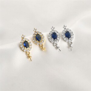 May include: A pair of gold and silver earring findings with a blue oval stone surrounded by clear rhinestones. The findings have a loop at the bottom for attaching a pearl or other charm.