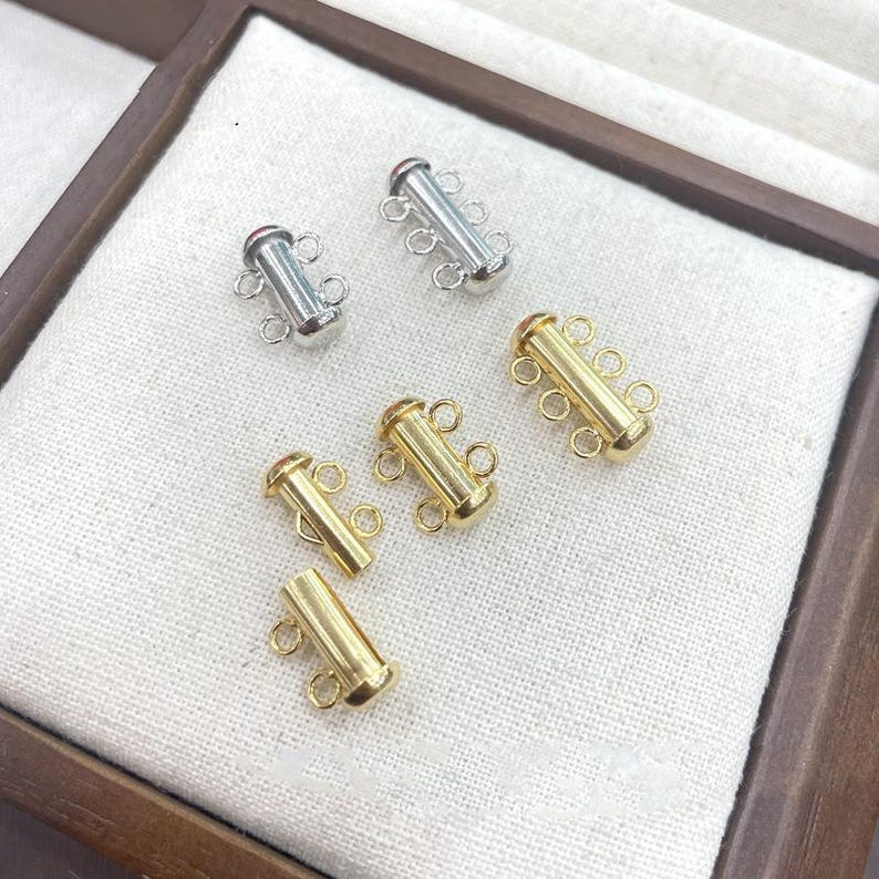 May include: A collection of six cylindrical jewelry clasps, including two silver-toned and four gold-toned pieces. Each clasp features multiple small circular loops attached to the side for connecting jewelry strands, with a smooth metallic finish.