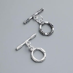 May include: Two silver-toned toggle clasps for jewellery making. Each set consists of a circular ring and a T-bar component. The metal surfaces feature a decorative, engraved pattern with darkened recessed areas to highlight the intricate design details.