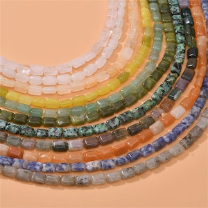 Puede incluir: Una hebra de cuentas de piedras preciosas de colores, con varios tonos de verde, azul, naranja y amarillo. Las cuentas son de forma rectangular y tienen un acabado pulido.