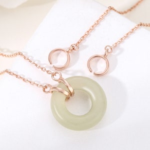 Puede incluir: Un collar de oro rosa con un colgante de jade verde claro en forma de círculo. El colgante tiene un diseño de doble anillo y está unido a una cadena delicada.