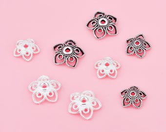 May include: Assortment of silver and black metal flower-shaped bead caps. The caps have a hole in the center for stringing beads.