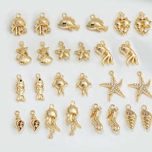 Può includere: Una collezione di ciondoli in metallo dorato con vari disegni di vita marina, tra cui stelle marine, cavallucci marini, conchiglie, meduse e pesci. I ciondoli sono decorati con strass trasparenti.