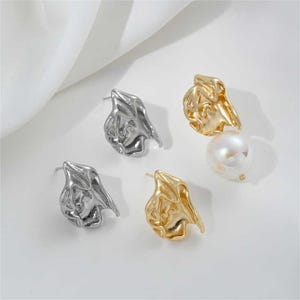 May include: A set of four earrings featuring abstract, organic shapes. Two earrings are silver and two are gold. One of the gold earrings has a pearl attached.