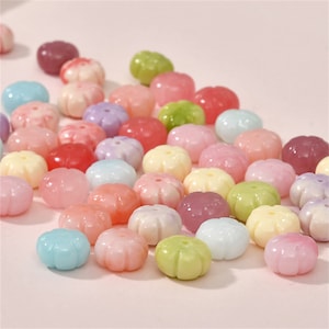 May include: Assortment of pastel-coloured plastic flower-shaped beads. The beads are in shades of pink, purple, blue, green, and yellow.