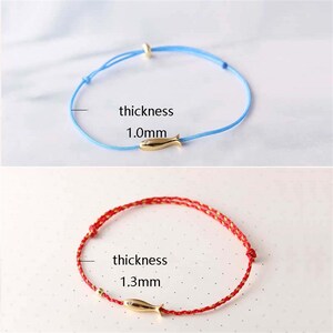 May include: Two bracelets with a gold fish charm. The top bracelet is light blue with a 1.0mm thickness. The bottom bracelet is red with a 1.3mm thickness.