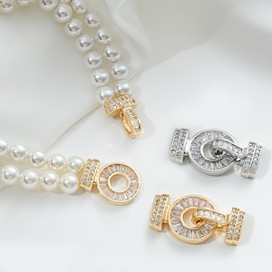 May include: Two gold and silver tone clasps with a circle design encrusted with clear cubic zirconia stones. The clasps are attached to a double strand of white faux pearl necklace.