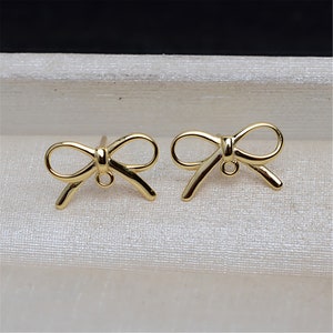 May include: A pair of gold bow-shaped earring studs. The earrings are made of metal and have a simple design.
