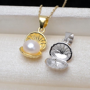 May include: Two gold and silver shell pendants with a pearl inside one of the shells. The pendants are on a white surface.