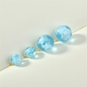May include: Four clear glass spheres with a light blue tint and white cloud designs inside. The spheres are arranged in a row from largest to smallest.