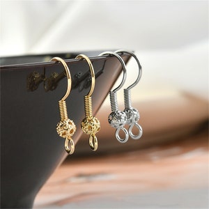 May include: Two gold and one silver earring hooks with a ball-shaped end. The ball has a textured design.