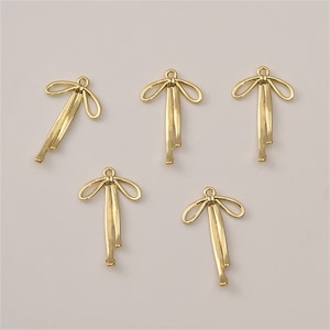 May include: Five gold-colored metal bow charms with a loop at the top for attaching to jewelry or other crafts.