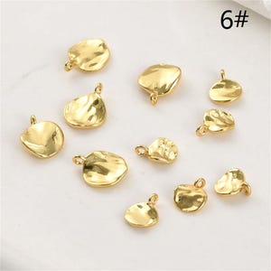 May include: A selection of gold-coloured, irregularly shaped charms with small loops for attaching to jewellery. The charms have a hammered texture and a shiny finish, ideal for crafting necklaces, bracelets, or earrings. The charms are scattered on a light background.