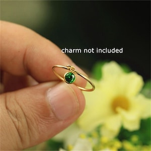 Puede incluir: Un anillo de oro con una pequeña piedra preciosa verde que cuelga de él. El anillo está en un dedo y el texto "charm not included" es visible sobre el anillo.