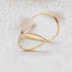 Può includere: Un paio di delicati orecchini dorati. Uno è a forma di goccia, l'altro è un cerchio aperto e curvo. Gli orecchini sono su uno sfondo morbido e strutturato, che ne evidenzia la semplice eleganza.