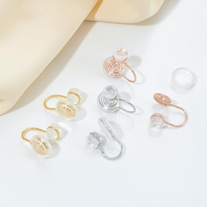 May include: Six pairs of non-pierced earrings in silver, gold, and rose gold. Each earring features a clear, round, swirl design.