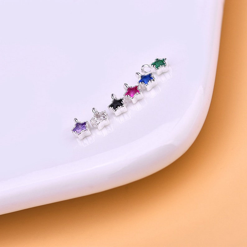 May include: A set of six silver star-shaped charms with different colored gemstones. The charms have a loop at the top for attaching to jewelry.