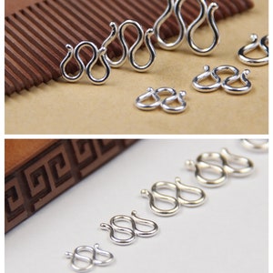 May include: A set of six silver-toned metal clasps in various sizes. The clasps are shaped like the number eight, with two loops connected together. The clasps are arranged in a row from largest to smallest.